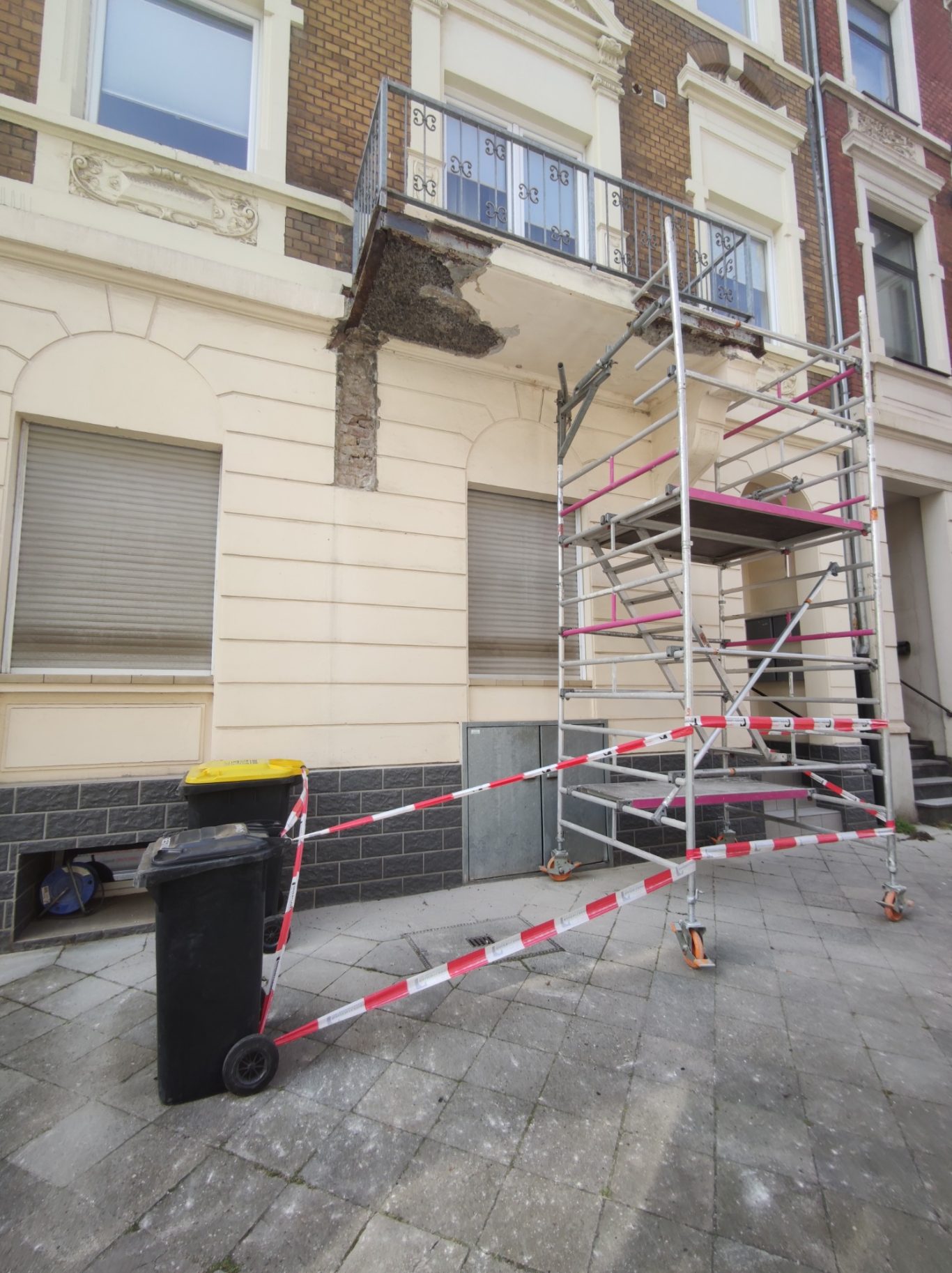 Baugerüst an einem Gebäude mit Mülltonne und Warnbändern.