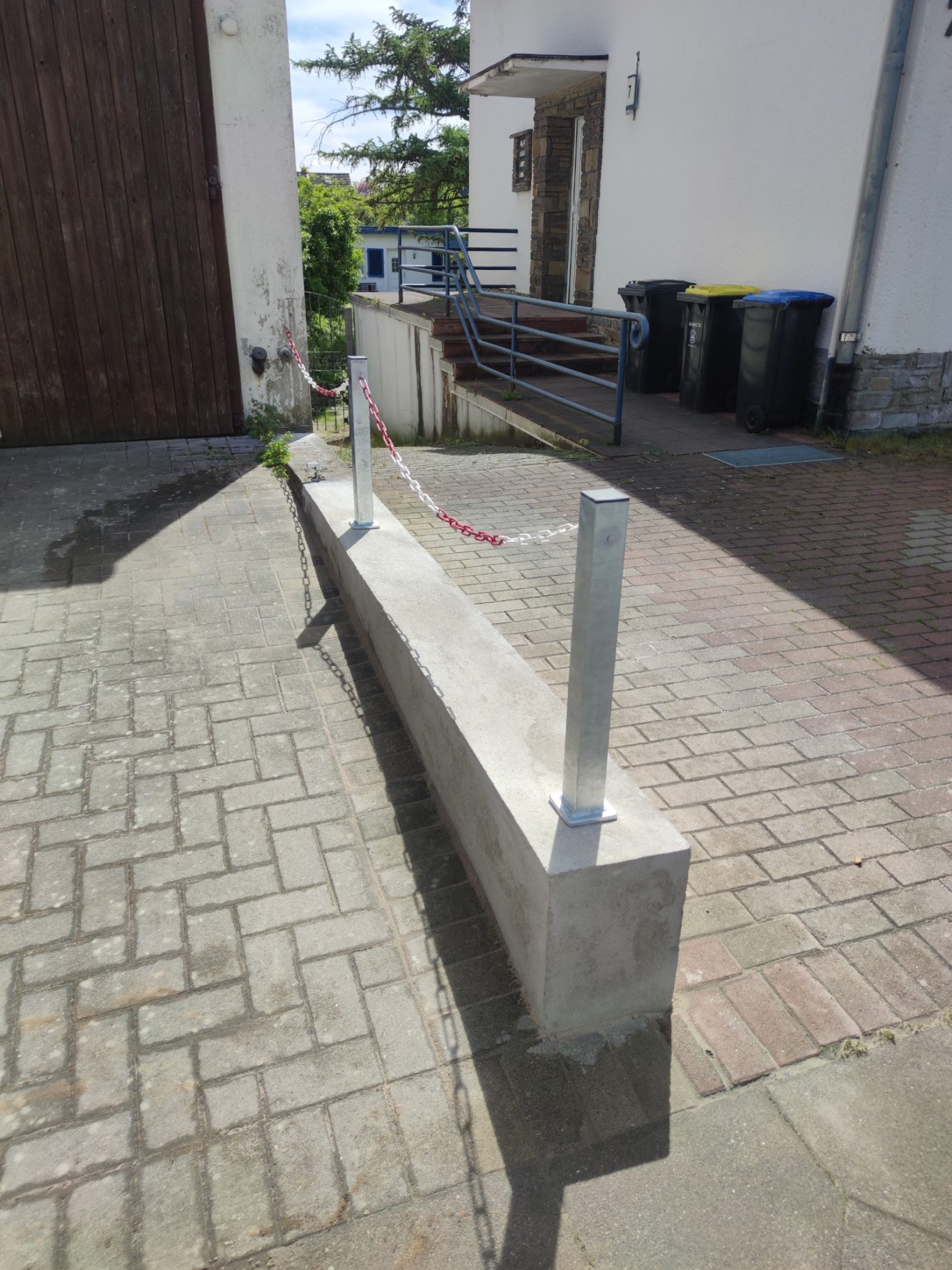 Betonbank mit Absperrband und Metallpfosten in einer schmalen Gasse.