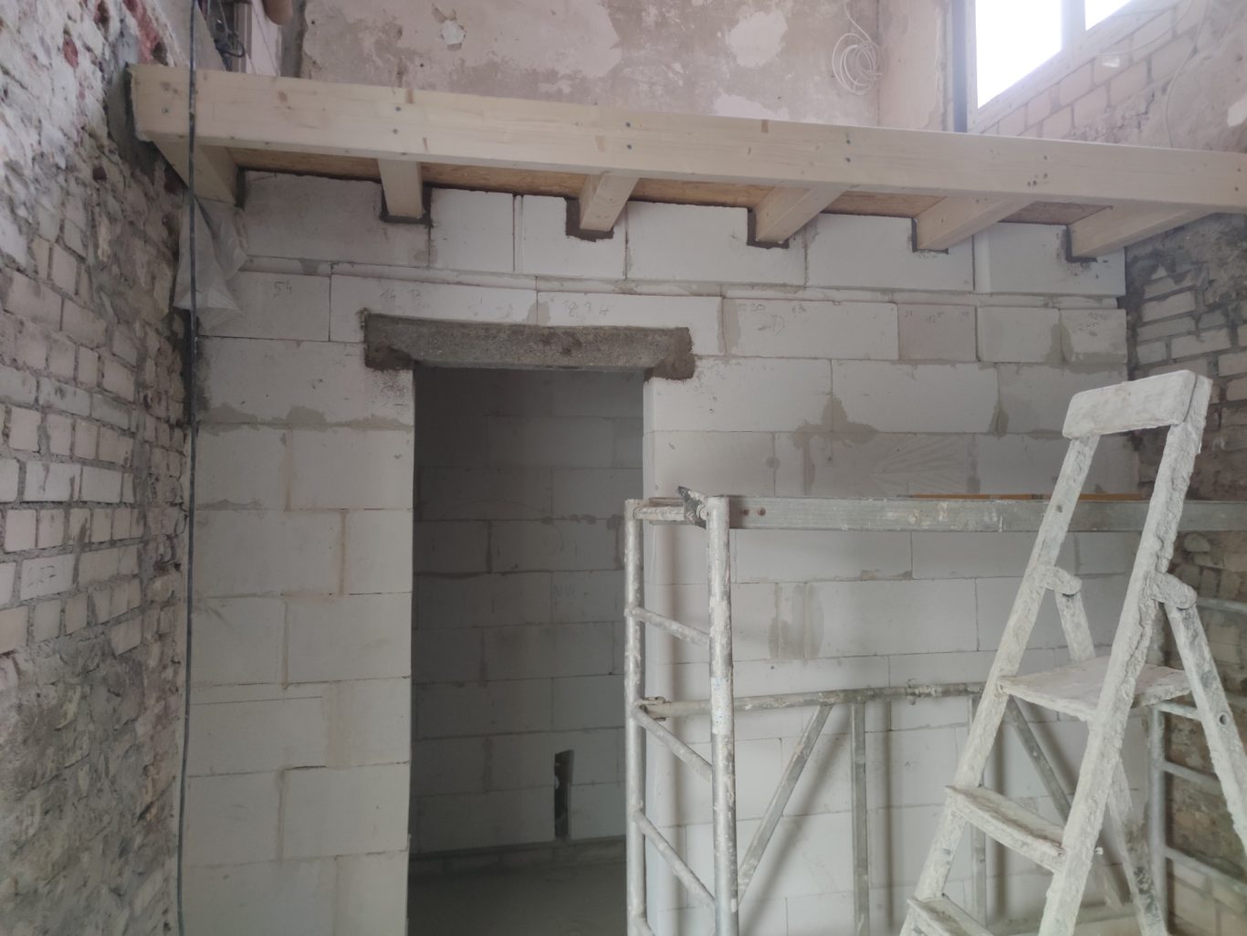 Rohbau eines Raums mit einer Holzstütze und einer Leiter im Vordergrund.