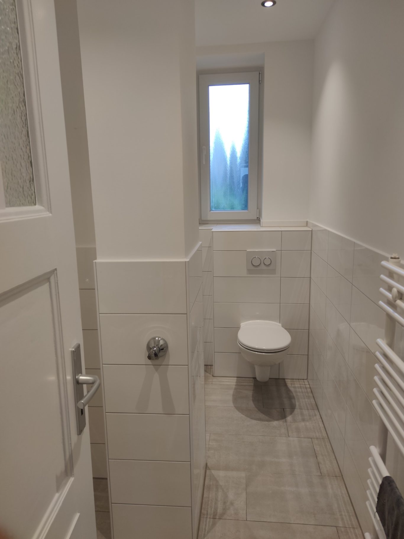 Klares Badezimmer mit Toilette, Fenstern und hellen Fliesenwänden.