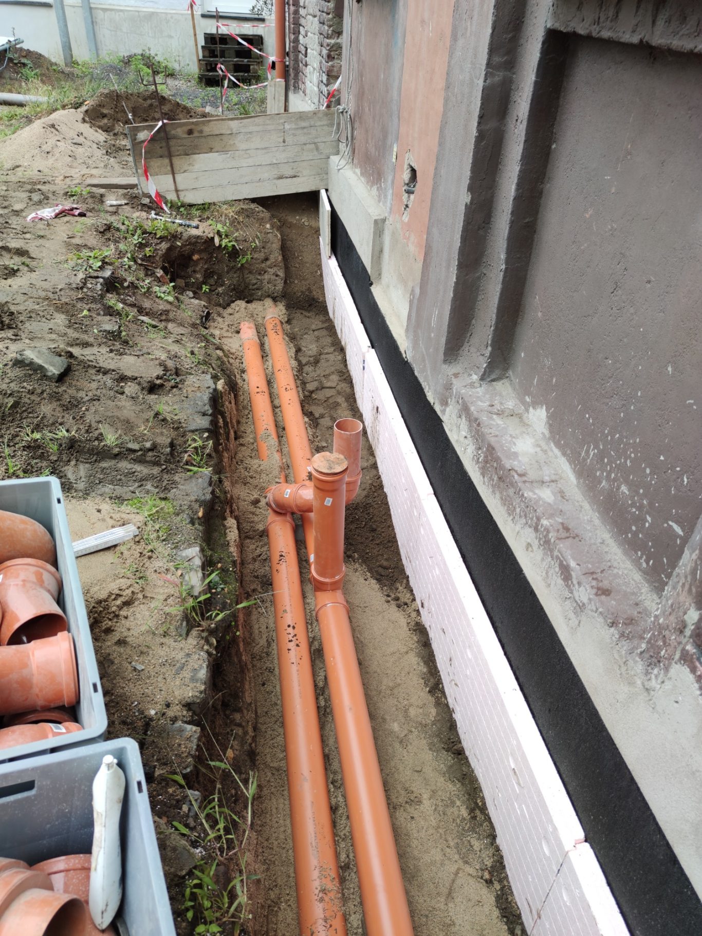 Orange Rohre verlegt im Boden neben einem Gebäude, umgeben von Erdreich.