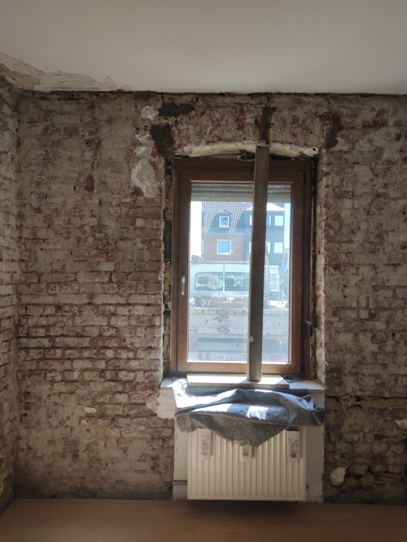 Unvollendeter Raum mit Ziegelwänden und einem Fenster über einer Heizungsanlage.